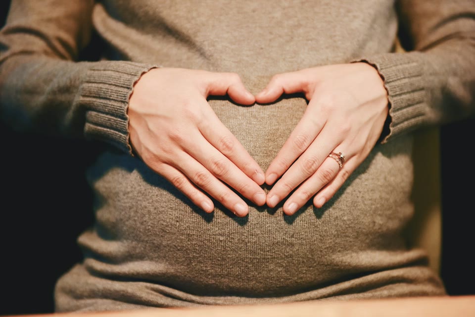 Pregnant person resting both hands on their abdomen