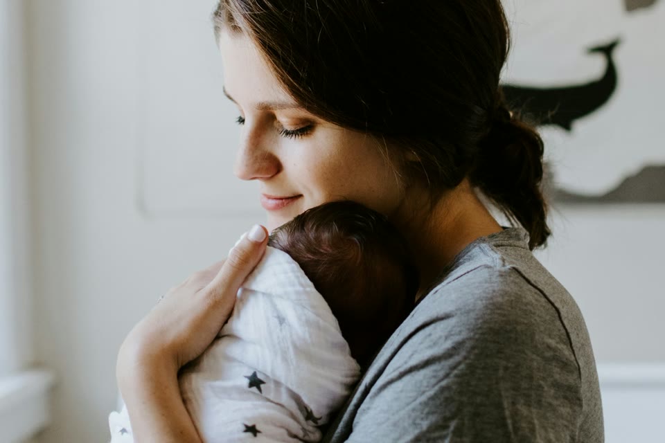 Mother holding a sleeping baby near a window